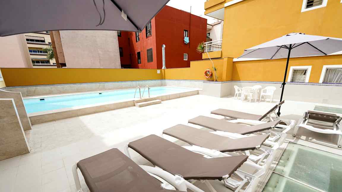 Utomhuspool med solstolar och parasoller på ett stenlagt område. (AI-genererad text)