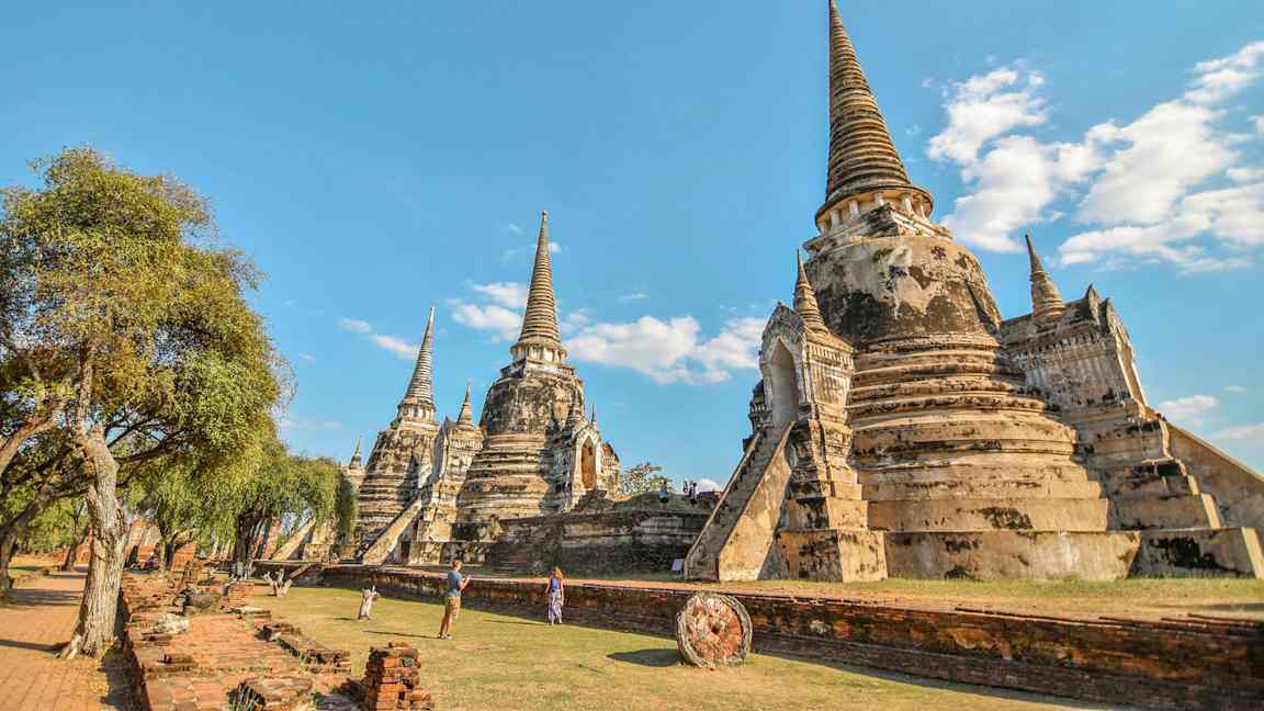 Bilden visar historiska buddhistiska tempelstupor i Ayutthaya, Thailand, mot en klar blå himmel. (AI-genererad text)