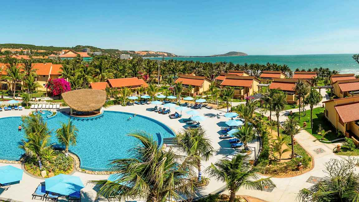 Semesteranläggning med stora byggnader med tegeltak, palmer och en pool i centrum. (AI-genererad text)