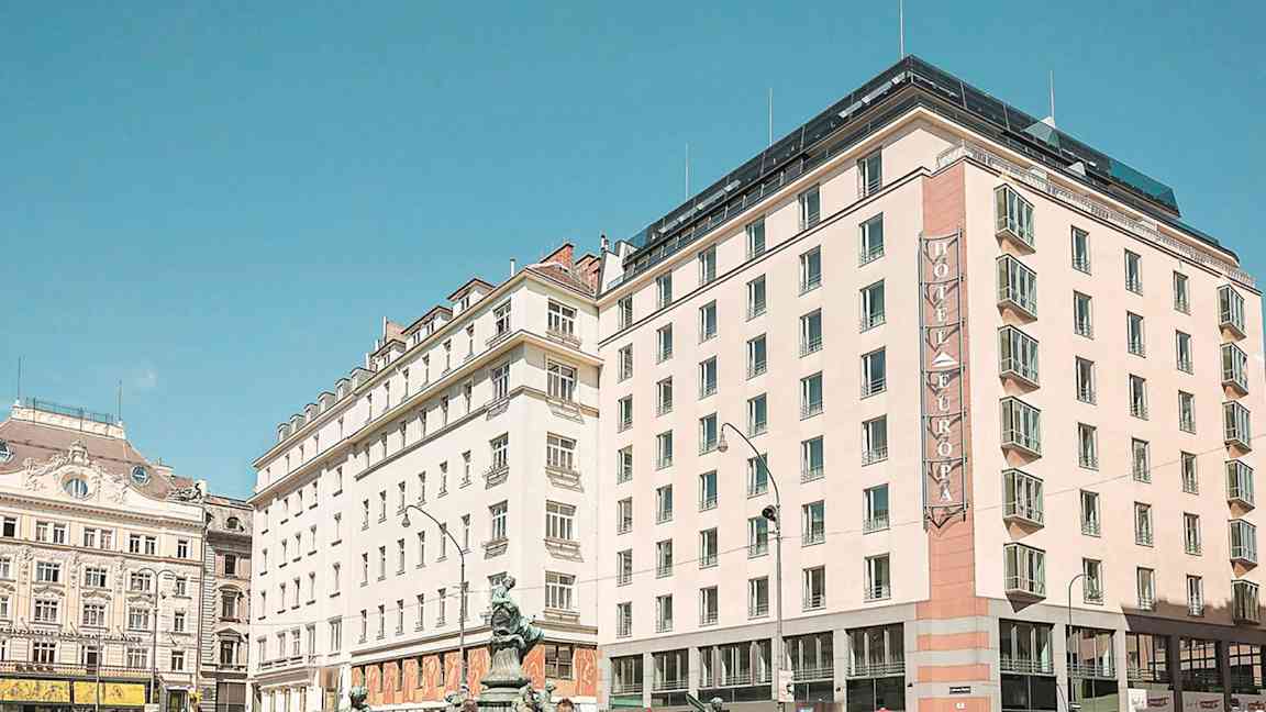 En stadsscen med flera byggnader, inklusive ett hotell med skylten "Hotel Europa", under en klar blå himmel. (AI-genererad text)