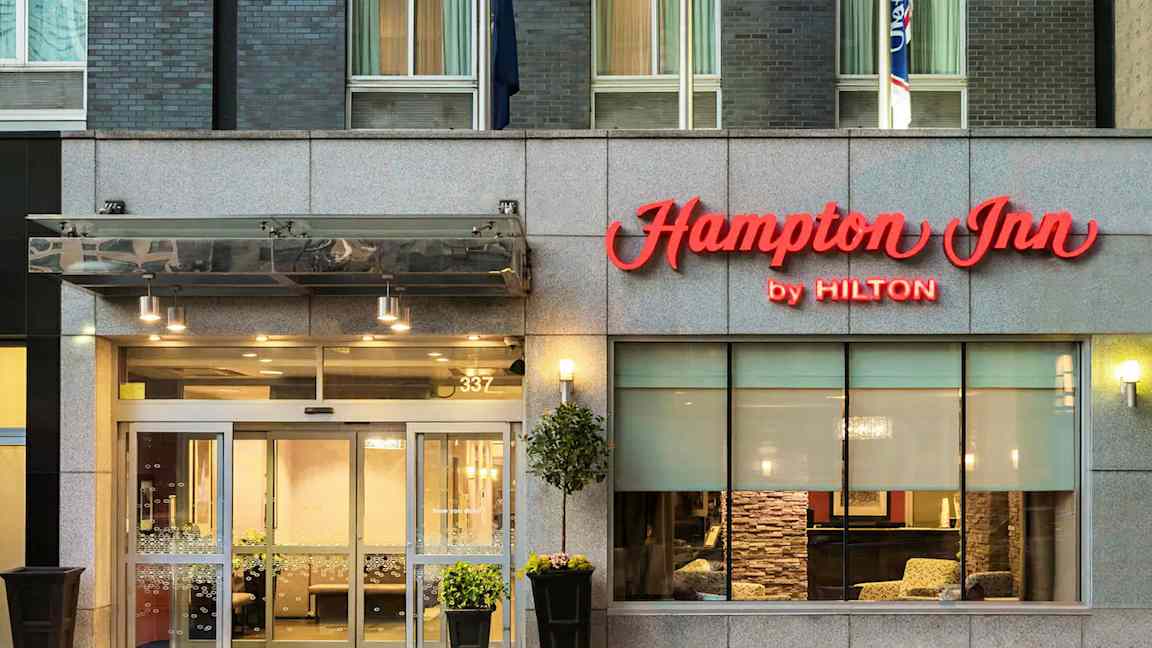 Hotellingång med skylt "Hampton Inn by Hilton" ovanför dörrarna. (AI-genererad text)
