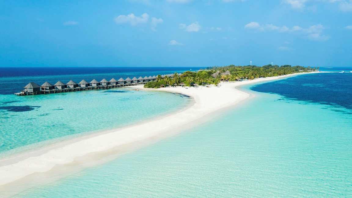 En tropisk strand med klarblått vatten, sand och palmer samt vattenbungalower på pelare. (AI-genererad text)