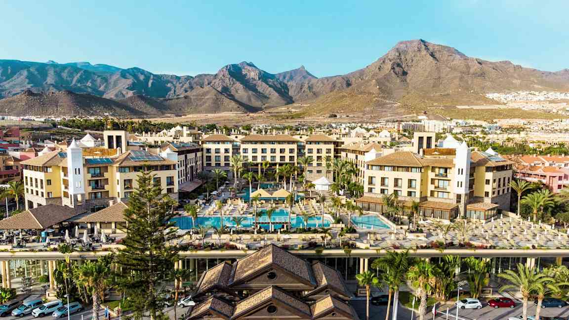 Hotellbyggnader med poolområde och berg i bakgrunden. (AI-genererad text)