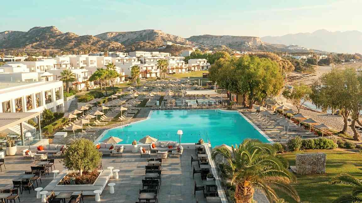 Luftbild av en semesteranläggning med pool, solstolar, byggnader och omgivande landskap. (AI-genererad text)