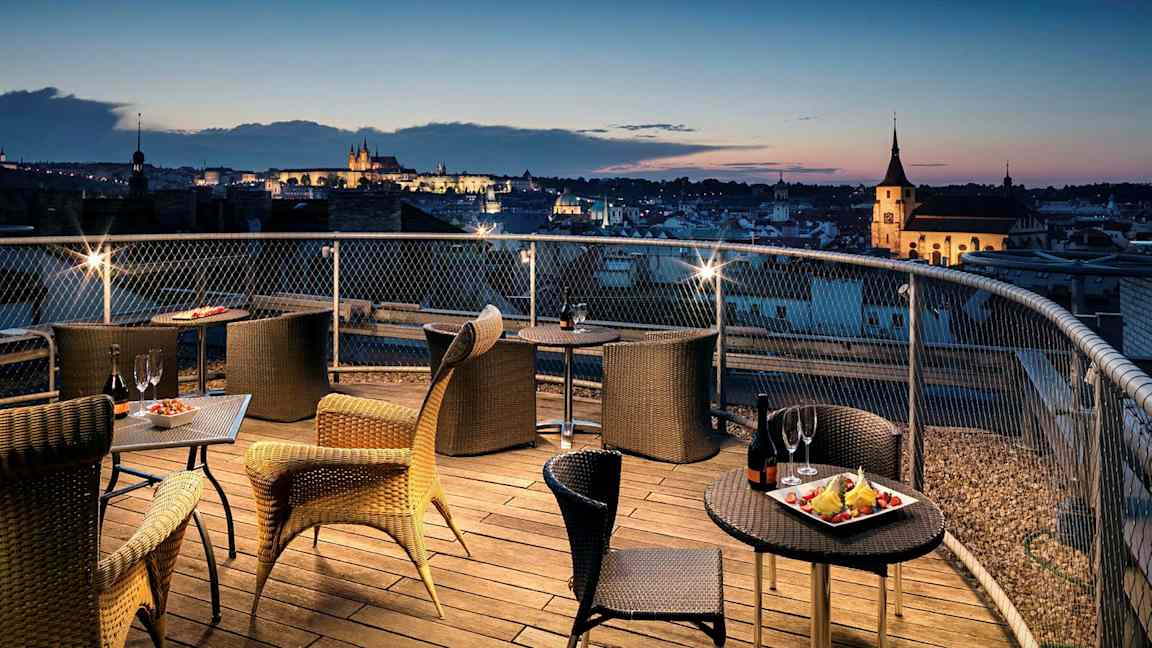 Terrass med sittplatser och utsikt över stad vid solnedgång. (AI-genererad text)