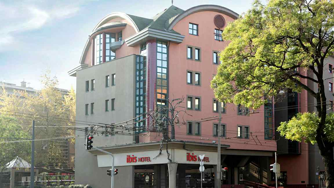 Ett hotell med en modern arkitektur och flera våningar, omgivna av träd och gata med trafikljus. (AI-genererad text)