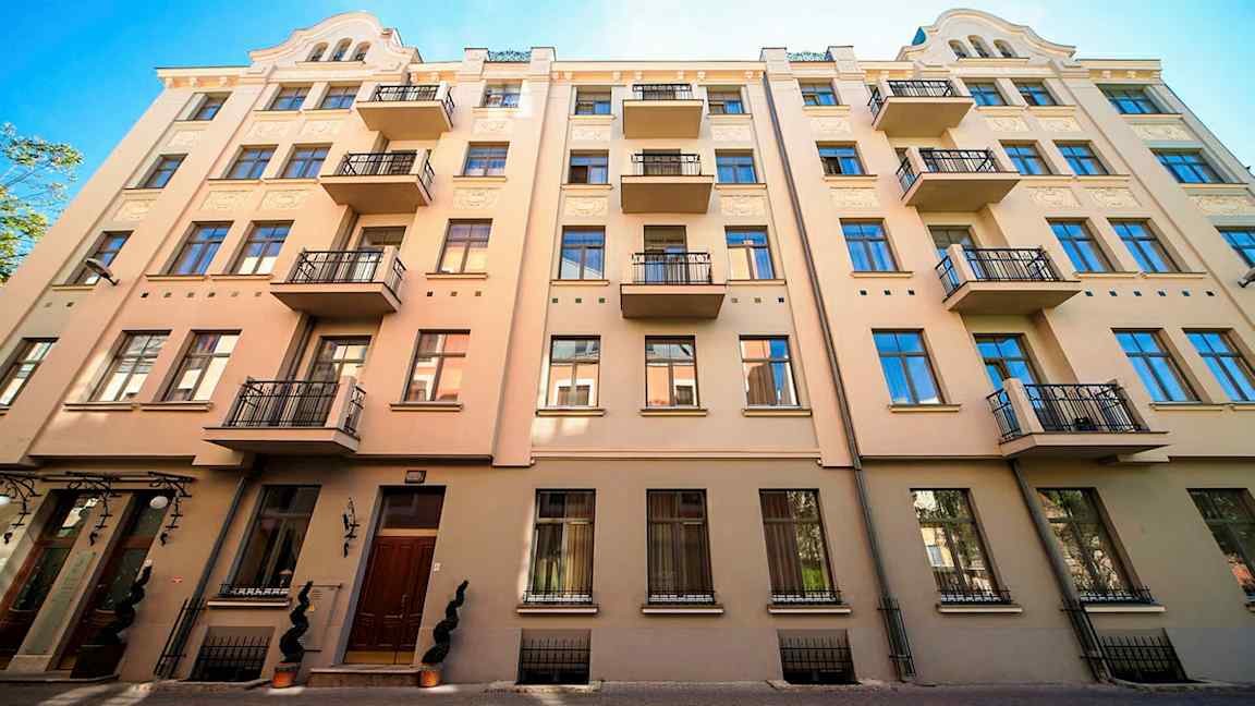 Fasad av en beige byggnad med flera balkonger och blå fönster. (AI-genererad text)