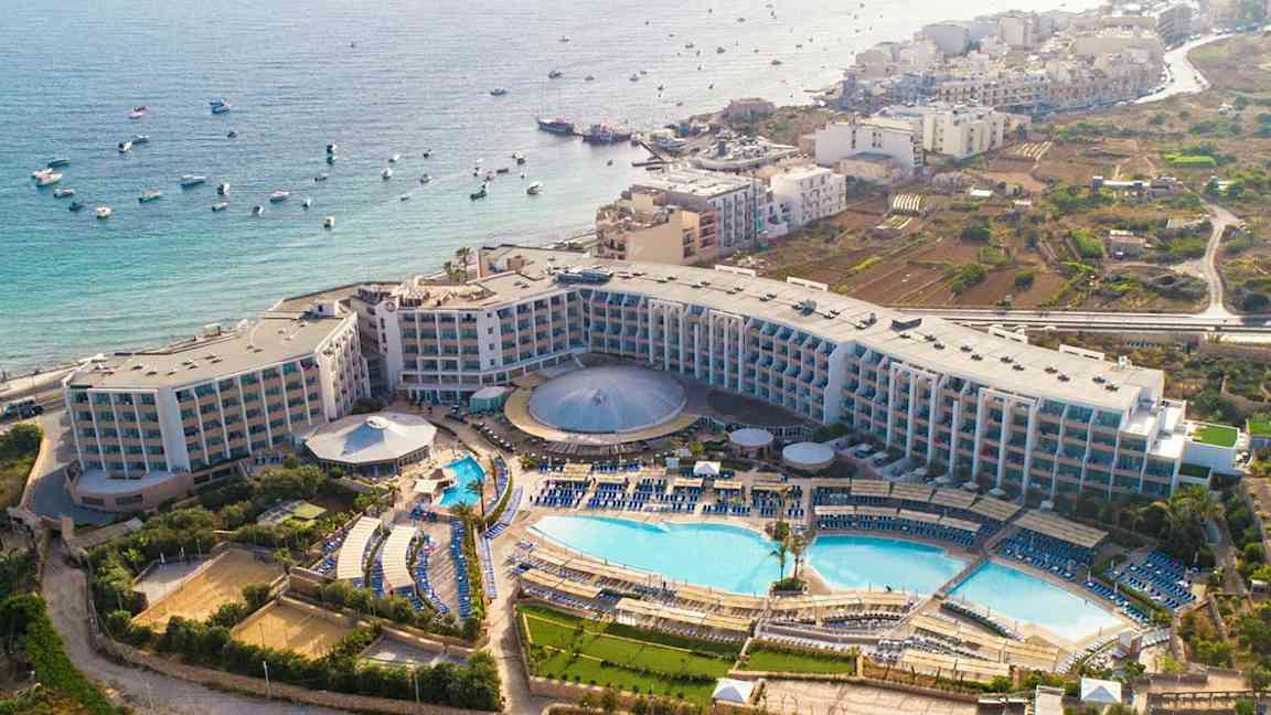 Flygfoto av ett hotellkomplex med pooler, grönområden och havsutsikt. (AI-genererad text)