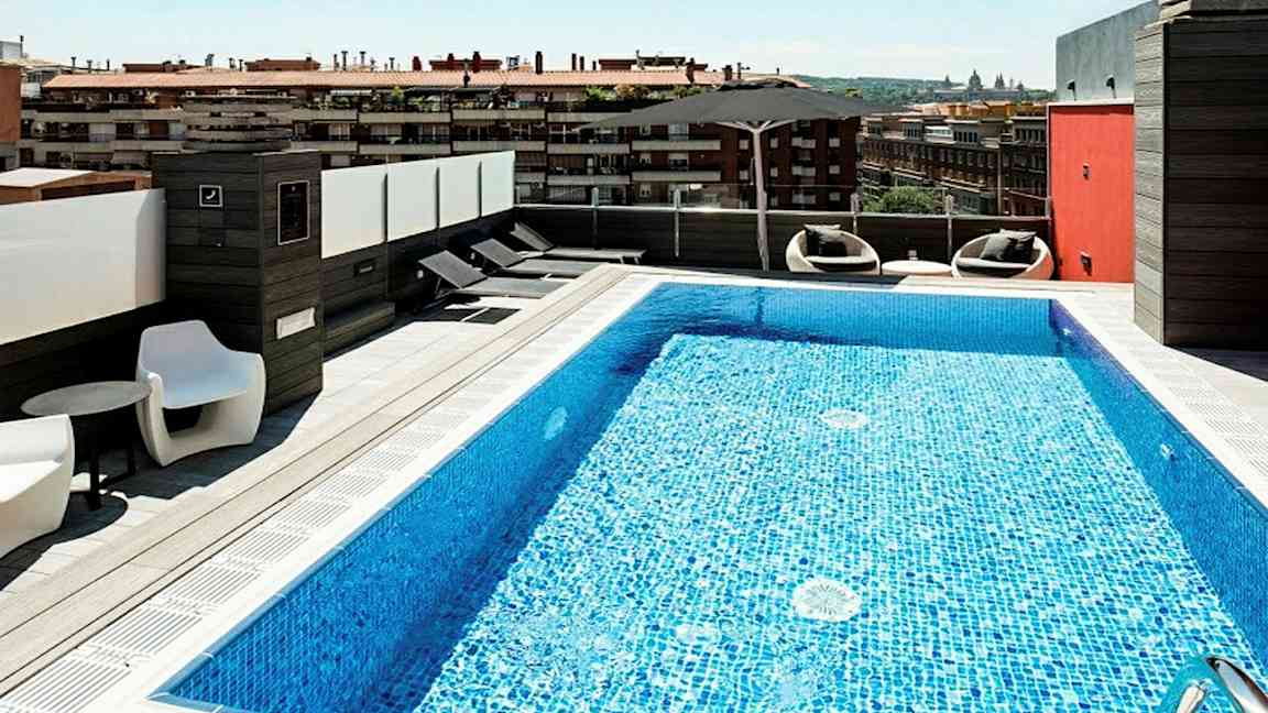 En takterrass med en pool och solstolar, med utsikt över en stadsmiljö. (AI-genererad text)