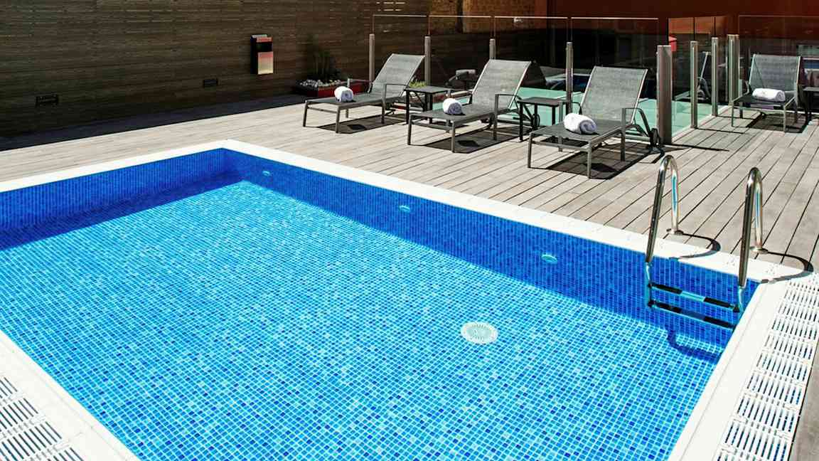 En blå mosaikpool med tillhörande solstolar på en trädäckad yta. (AI-genererad text)