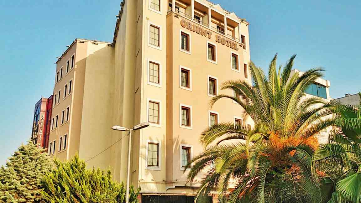 En hotellbyggnad med flera våningar. Det finns palmer och gröna träd framför byggnaden. (AI-genererad text)