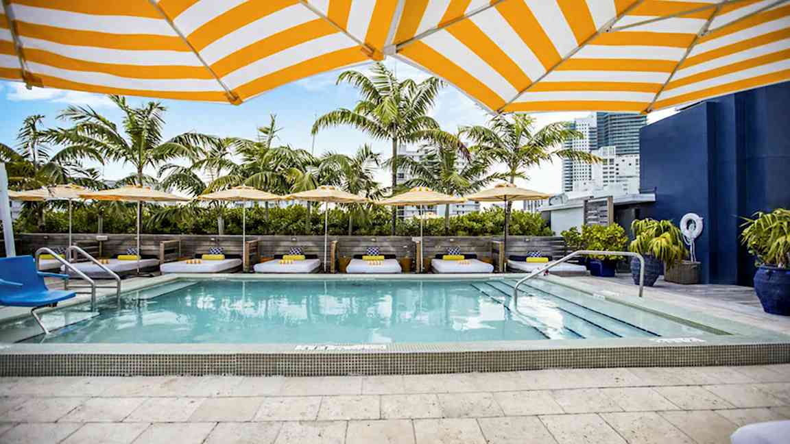 Ett poolområde med solstolar, parasoller och palmer i bakgrunden. (AI-genererad text)