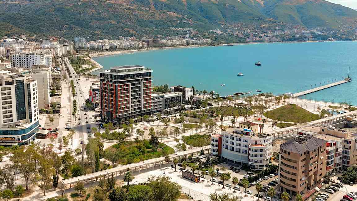 Utsikt över en kuststad med byggnader, grönområden och en pir vid havet. (AI-genererad text)