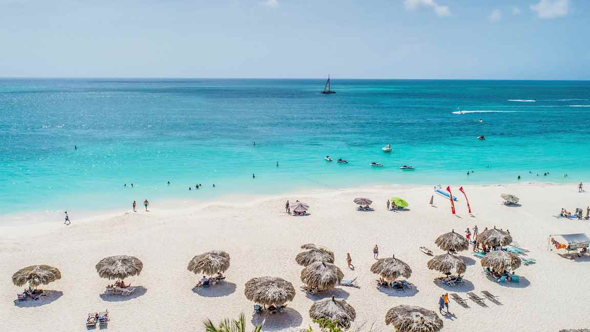 En sandstrand med parasoller och människor som solar och badar i en blå havsmiljö. (AI-genererad text)
