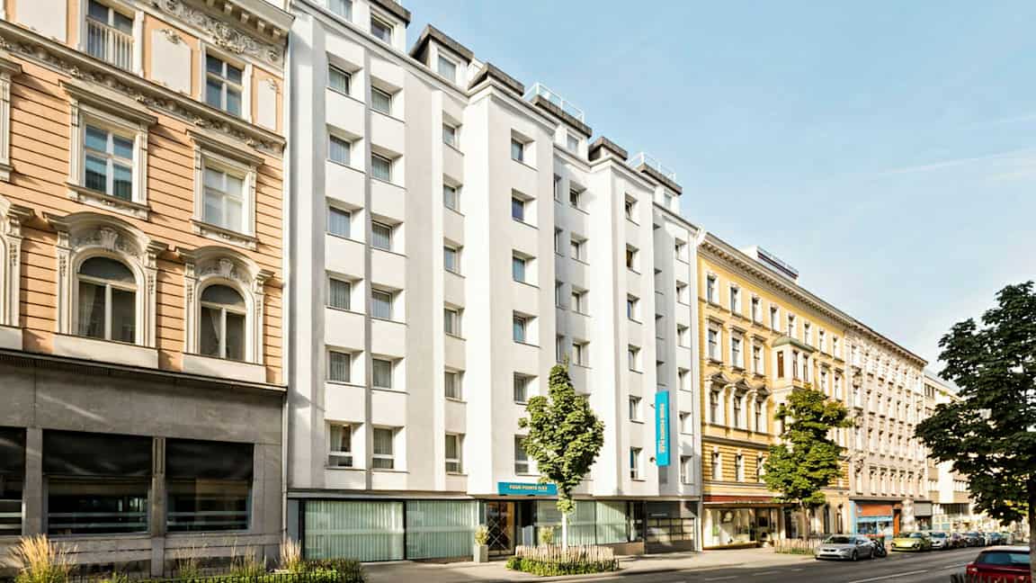 En stadsgata med byggnader från olika årtionden, inklusive ett hotell med vit fasad. (AI-genererad text)