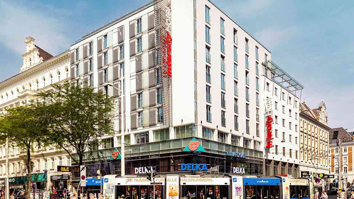 En flerfärgad spårvagn framför ett modernt hotell i stadslandskap. (AI-genererad text)