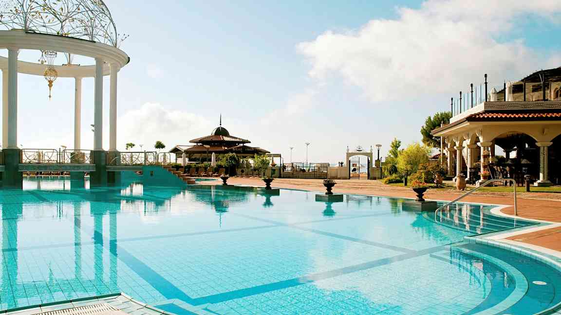 En utomhuspool med en dekorerad paviljong och omgivning av byggnader i medelhavsstil. (AI-genererad text)