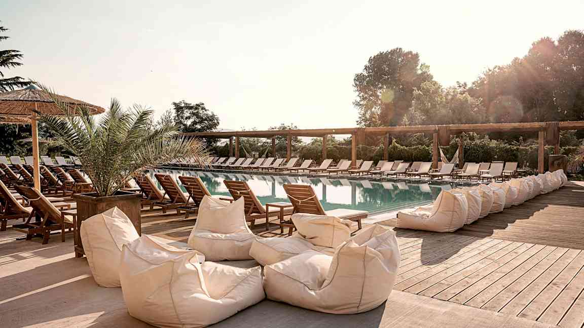 En utomhuspool omgiven av solstolar och sittsäckar. (AI-genererad text)