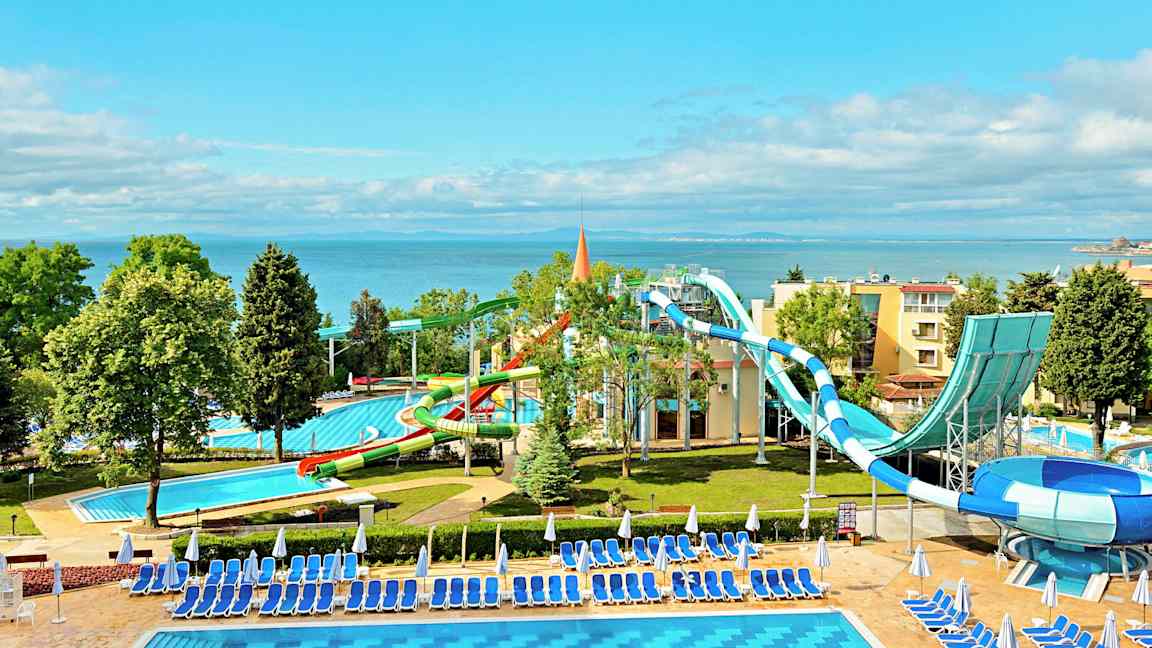 En vattenpark vid havet med vattenrutschbanor och pooler omgivna av solstolar och parasoller. (AI-genererad text)