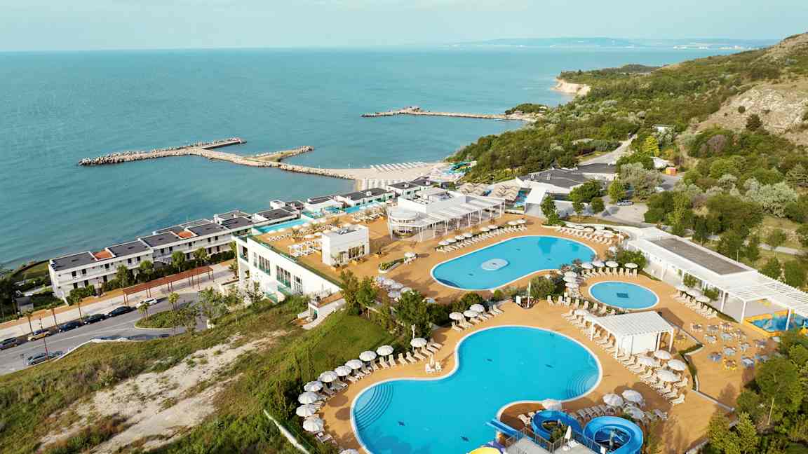 Bild av en resort vid havet med pooler, solstolar och en grönskande omgivning. (AI-genererad text)