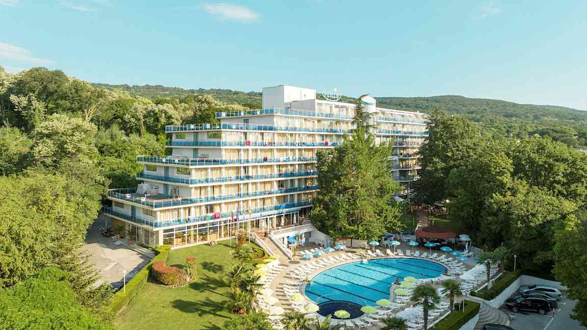 Bild av ett hotell med flera våningar och balkonger, omgiven av frodig grönska. En pool med solstolar ligger i förgrunden. (AI-genererad text)