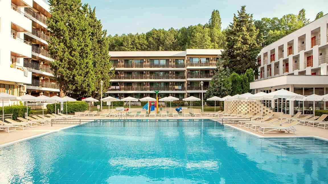 Utomhuspool med solstolar och parasoller, omgiven av moderna byggnader och grönska. (AI-genererad text)