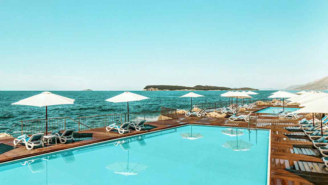 En swimmingpool vid havet, omgivet av solstolar och parasoller. (AI-genererad text)