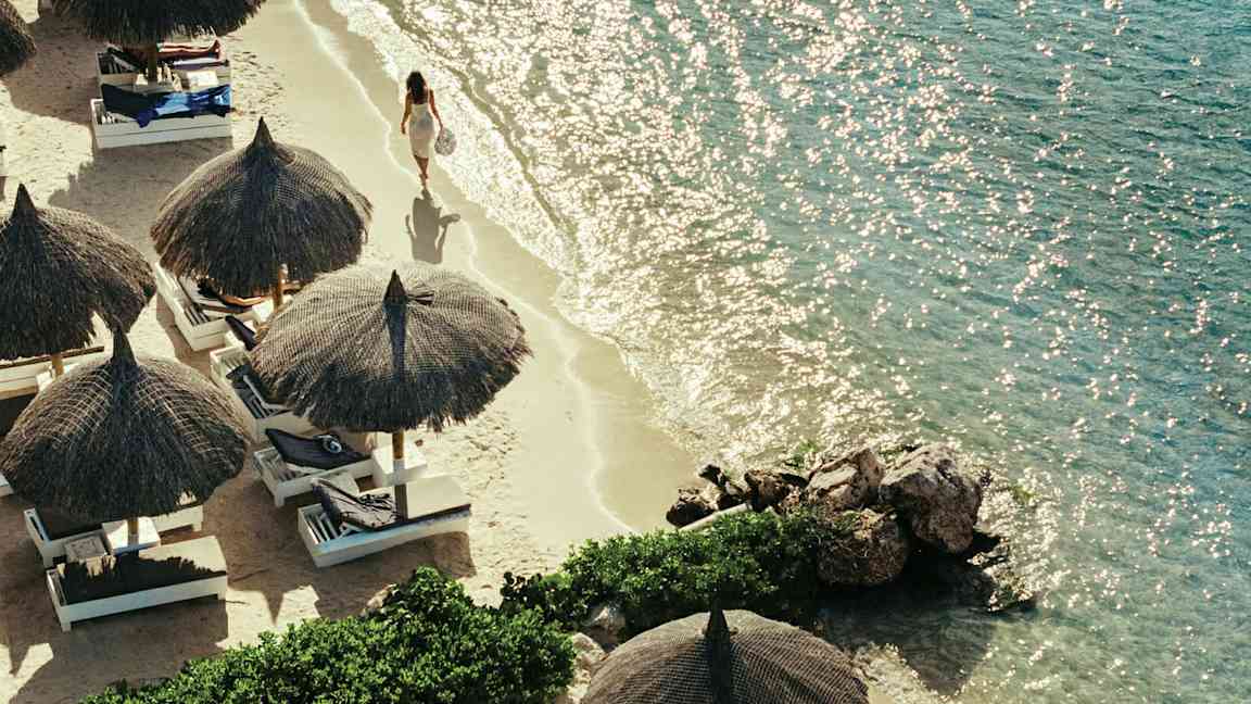 En strand med strandparasoller och solbäddar, samt en person som promenerar vid vattenkanten. (AI-genererad text)