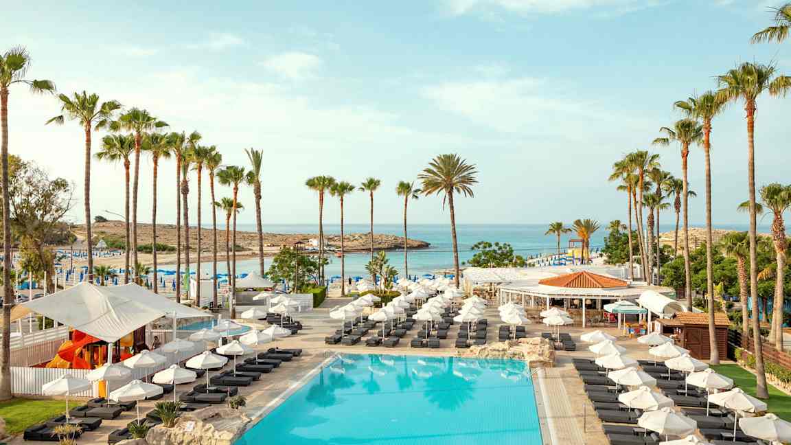 Bild av en pool med solstolar, parasoller och palmer vid en strand. (AI-genererad text)