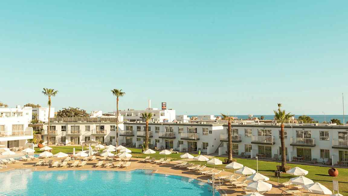 En semesterort med pool, solstolar, parasoller och omgivande byggnader. (AI-genererad text)