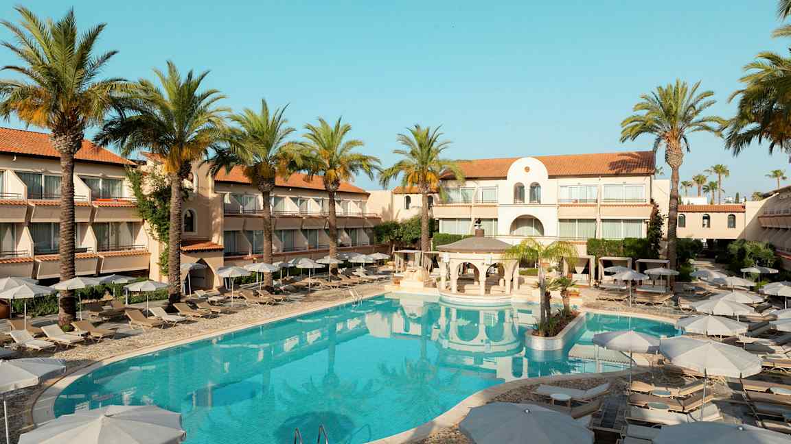 Hotellbyggnad med solstolar och parasoller kring en utomhuspool, omgivna av palmer. (AI-genererad text)