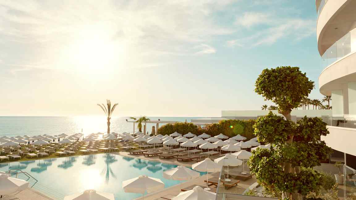 En utomhuspool med solstolar och parasoller, havet i bakgrunden. (AI-genererad text)