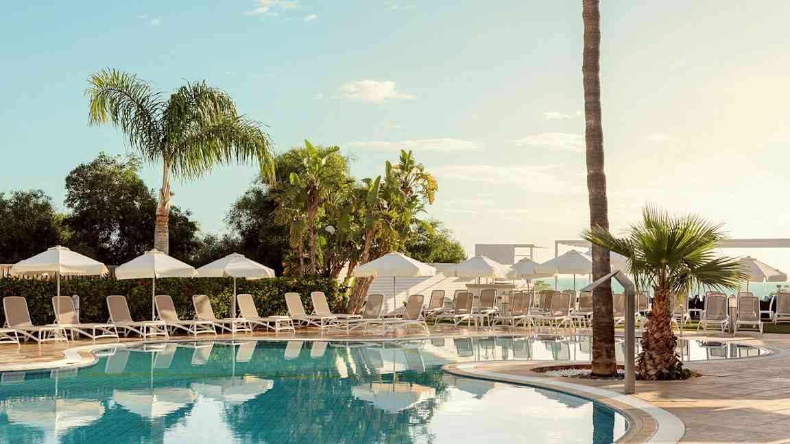 En utomhuspool omgiven av solstolar, parasoller och palmer. (AI-genererad text)