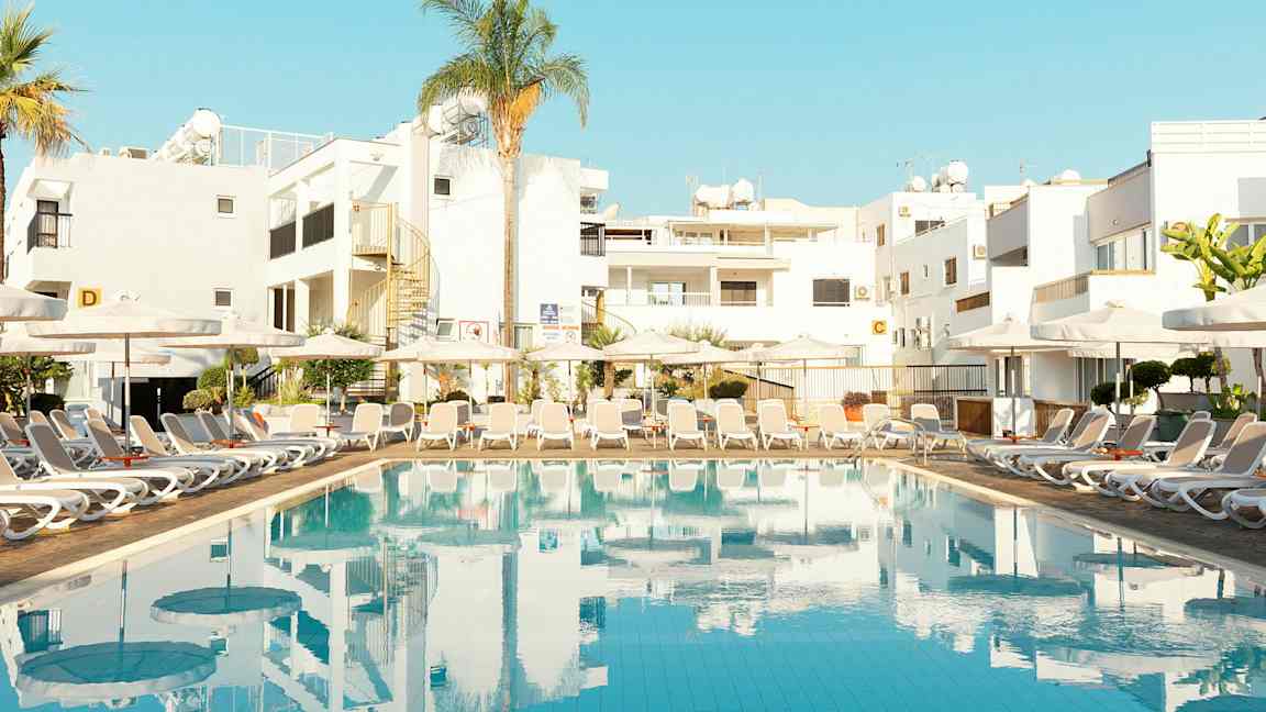 Pool med solstolar och byggnader i bakgrunden. (AI-genererad text)