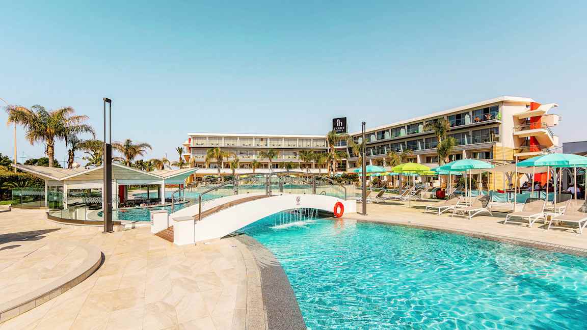 Bild av en pool, med en liten bro och hotellbyggnad i bakgrunden. (AI-genererad text)