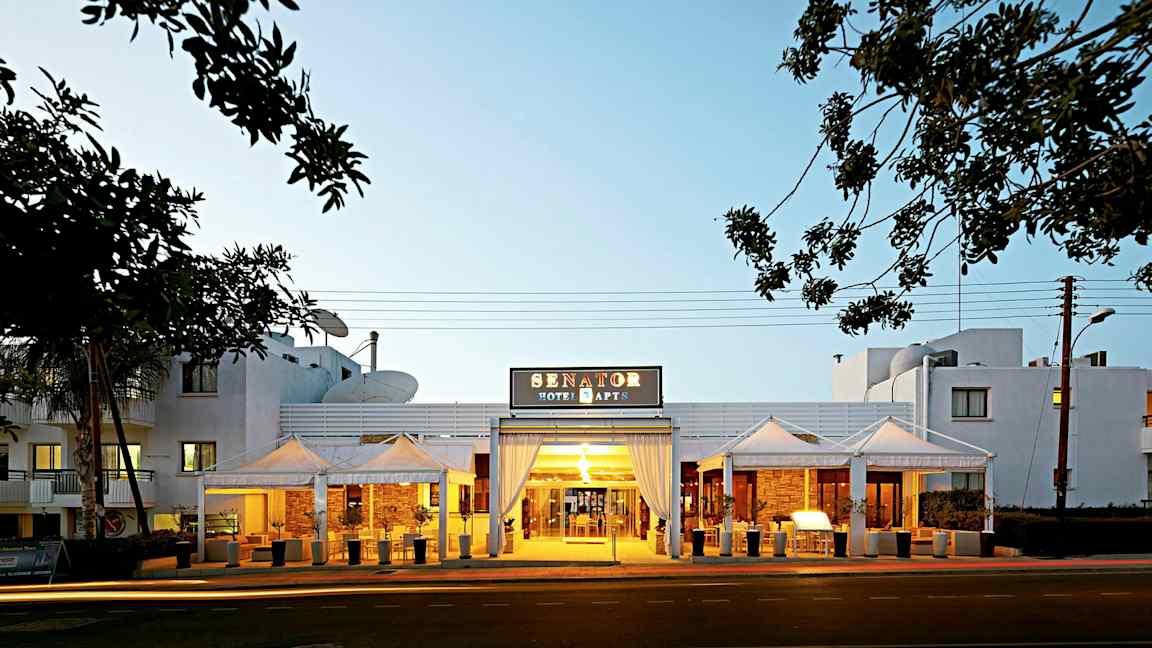 Entrén till Senator Hotel Apartments med kvällsbelysning. (AI-genererad text)