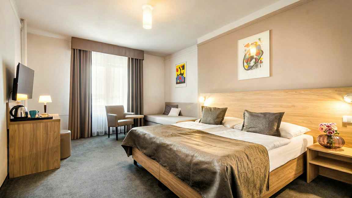 Ett hotellrum med en stor dubbelsäng, ett bord med två stolar och en väggmonterad TV. (AI-genererad text)