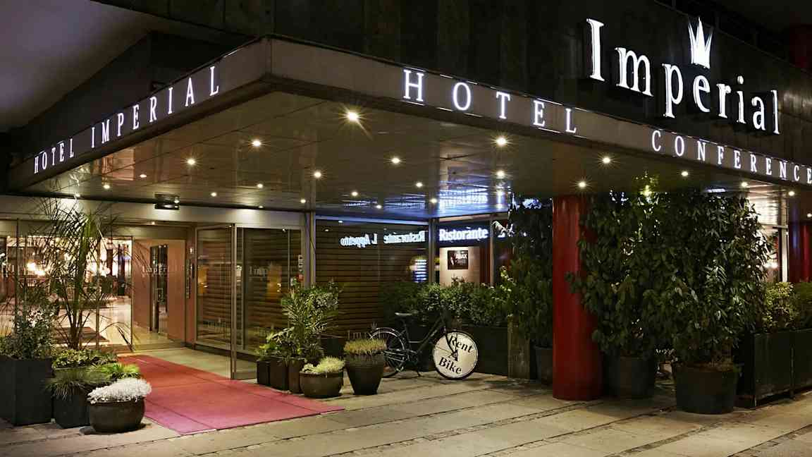 Entrén till Hotel Imperial Conference med glasdörrar, växter i krukor och en cykel med skylten 'Rent a Bike'. (AI-genererad text)