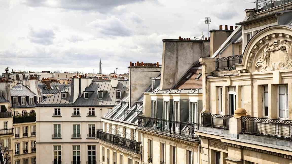 Bild på parisiska byggnader med typiska tak, med Eiffeltornet synligt i bakgrunden. (AI-genererad text)