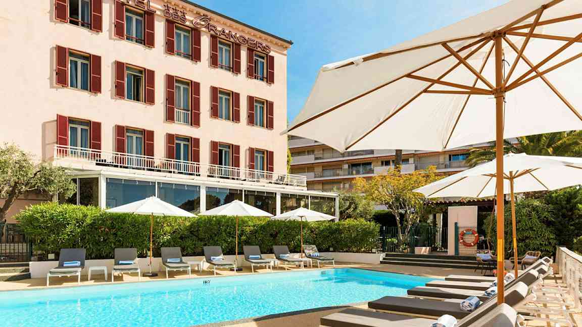 Hotellbyggnad med pool och solstolar framför. (AI-genererad text)