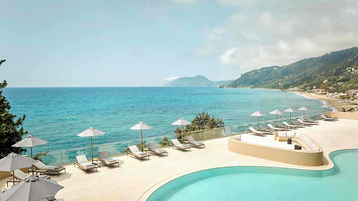 Utsikt över en pool och hav med solstolar och parasoller på en terrass. (AI-genererad text)