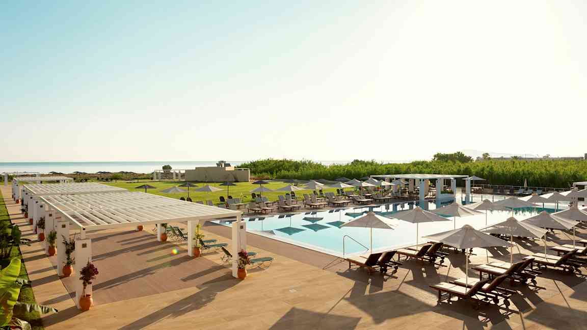 En utomhuspool med solstolar och parasoller på ett hotellområde vid havet. (AI-genererad text)