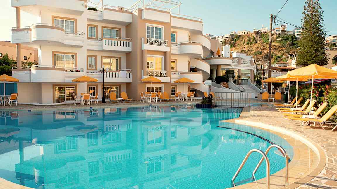 Bild av ett hotell med en pool och solstolar framför byggnaden. (AI-genererad text)