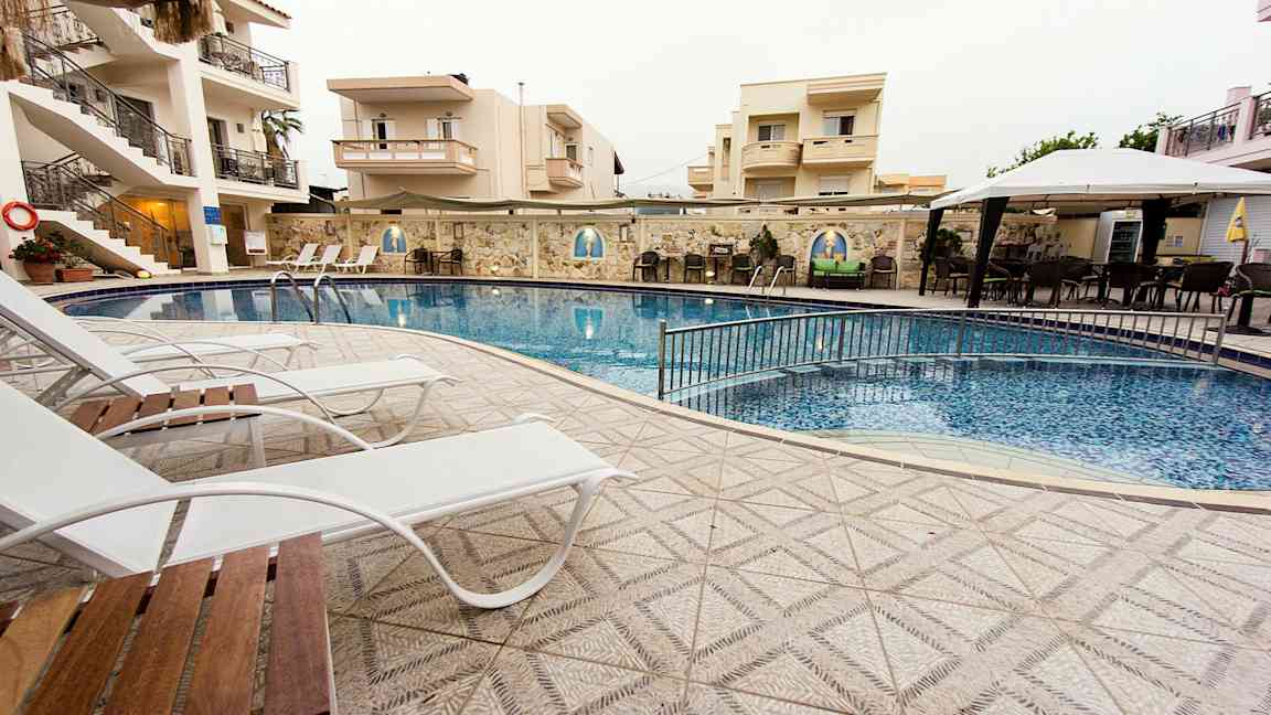 Utomhuspool vid hotell, omgiven av solstolar och byggnader. (AI-genererad text)
