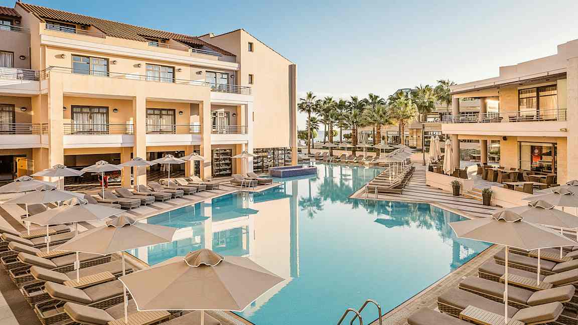 Bild av ett hotellområde med en pool och solstolar, omgivna av byggnader med balkonger och palmer. (AI-genererad text)