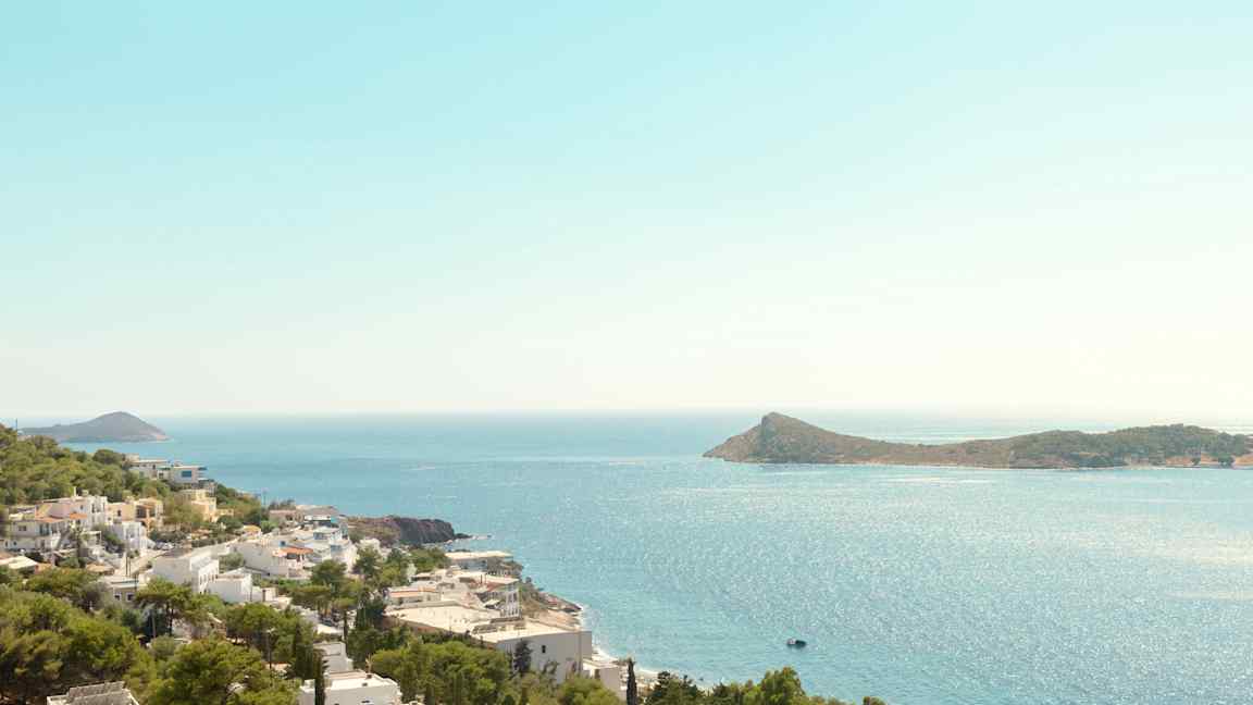 Utsikt över kustlinje med vita byggnader och gröna träd, hav och en ö i bakgrunden. (AI-genererad text)