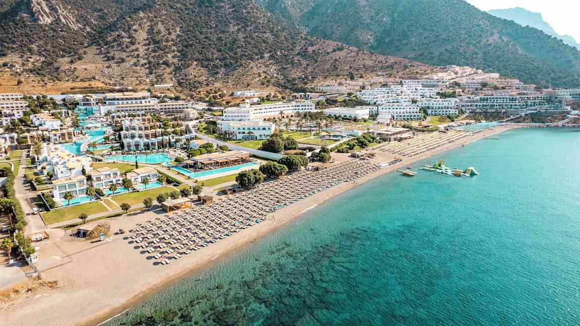 Flygfoto av en kustlinje med hotellkomplex vid stranden, pooler och solstolar. (AI-genererad text)