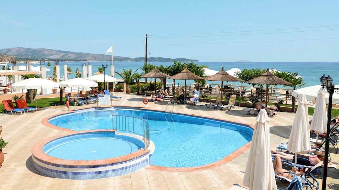 Poolområde vid havet med solstolar och parasoller omgivna av grönska. (AI-genererad text)