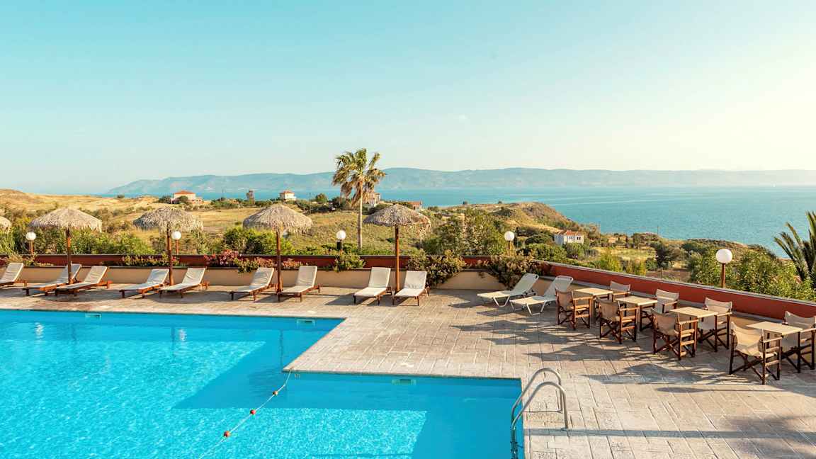 Bild av en utomhuspool med solstolar och parasoll, omgiven av grönska och med utsikt över havet. (AI-genererad text)