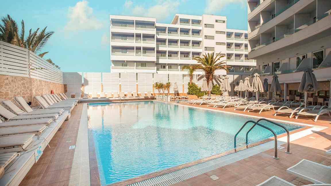 Hotellpool med solsängar och parasoller på omgivande terrass. (AI-genererad text)